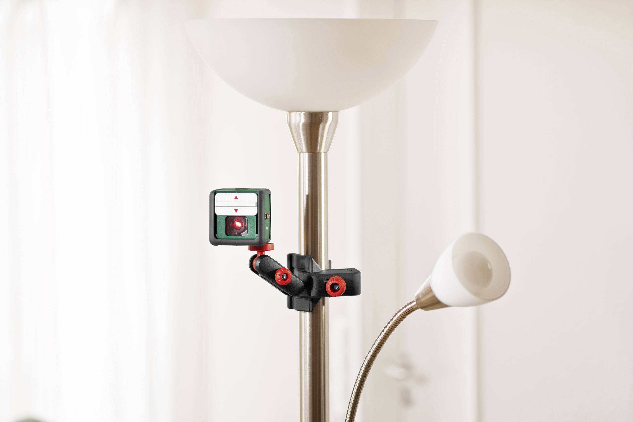 Une caméra est fixée à un lampadaire. La pièce est bien éclairée avec des rideaux blancs en arrière-plan.