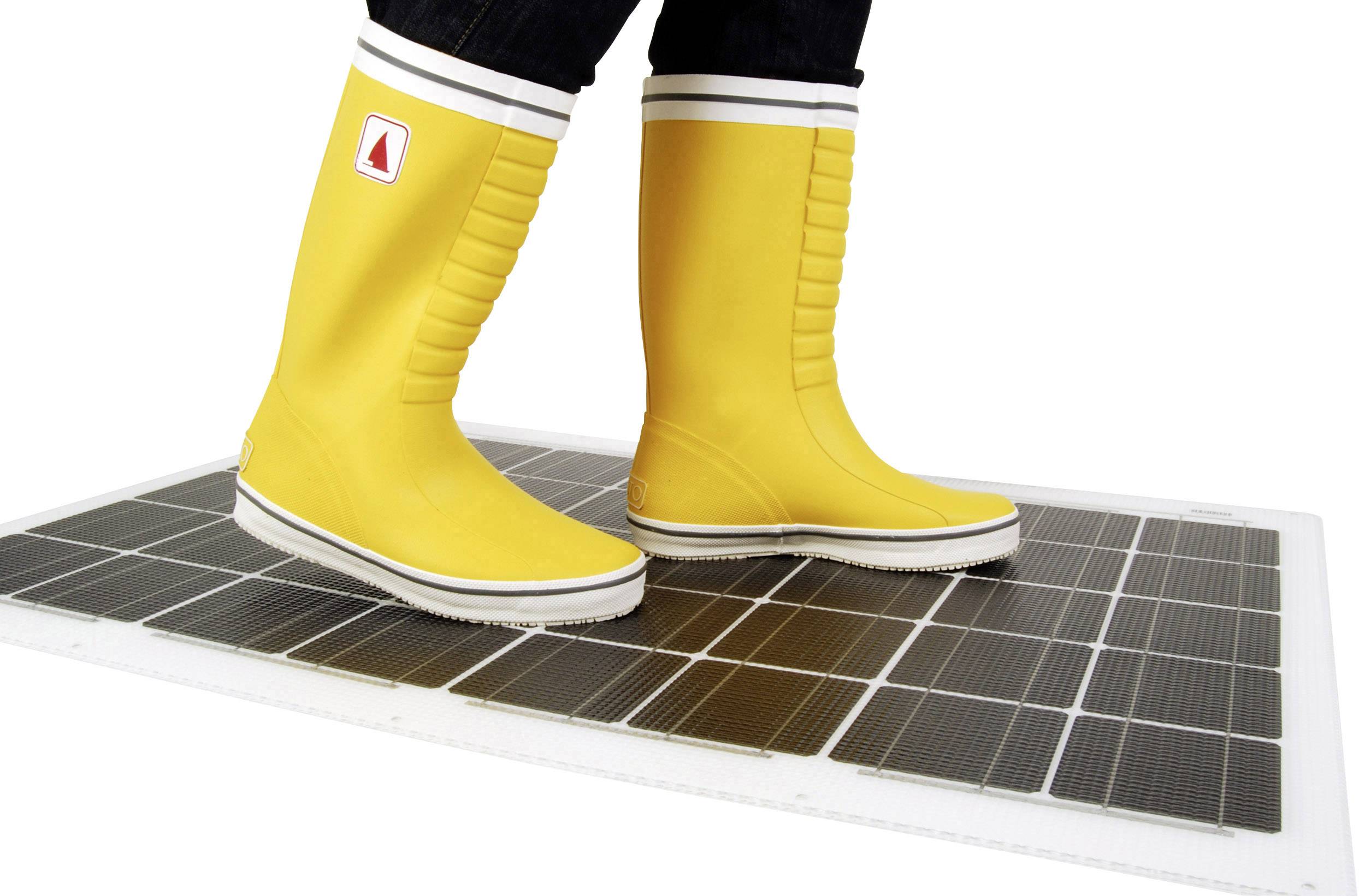 Une personne portant des bottes en caoutchouc jaunes se tient debout sur un panneau solaire.