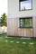 Un bâtiment moderne avec des éléments en bois, de grandes fenêtres et une prairie verte, entouré d'arbres. Ambiance détendue et proche de la nature.