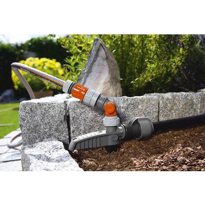 Un tuyau d'arrosage est raccordé à une pompe à eau installée dans un jardin, à côté de dalles de pierre et de paillis.