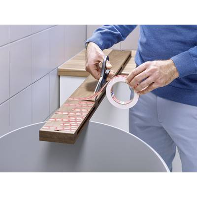 Une personne coupe un morceau de ruban adhésif double face d'un rouleau avec des ciseaux pour le coller sur une planche en bois.