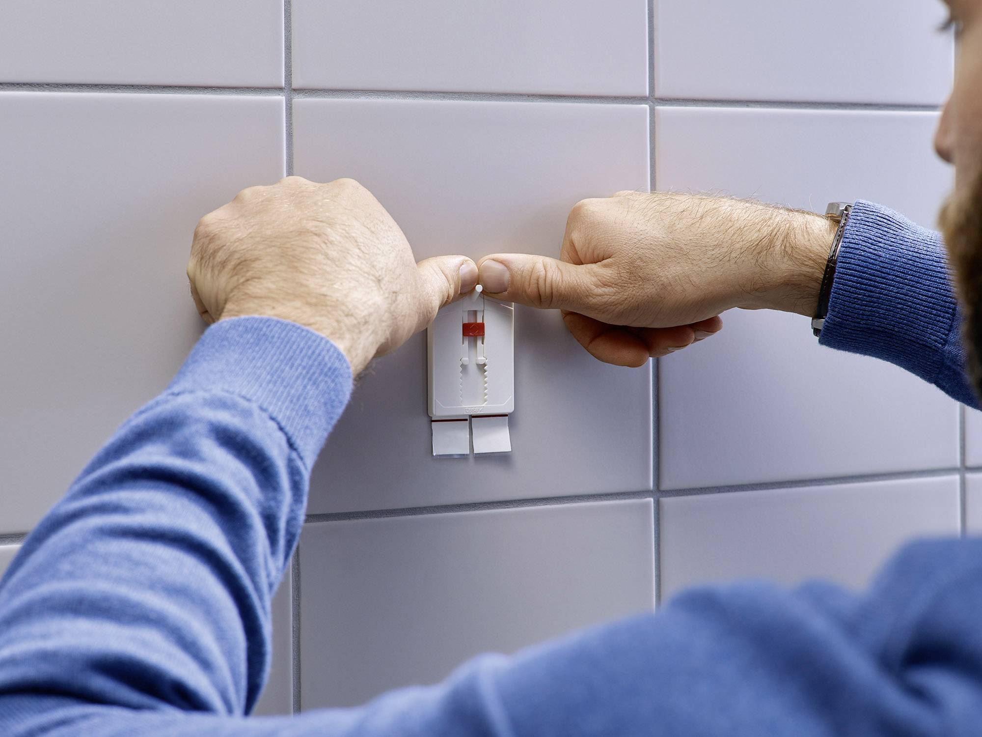 Une personne retire du ruban adhésif double face d'un rouleau blanc fixé à un mur carrelé.