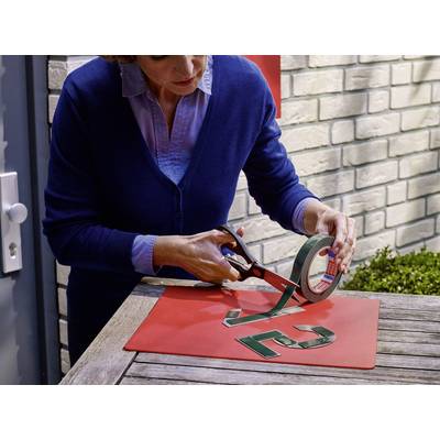 Une personne coupe du ruban adhésif avec des ciseaux sur une table en bois. Sur la table sont posés des chiffres verts, une planche rouge et un mur de briques en arrière-plan.
