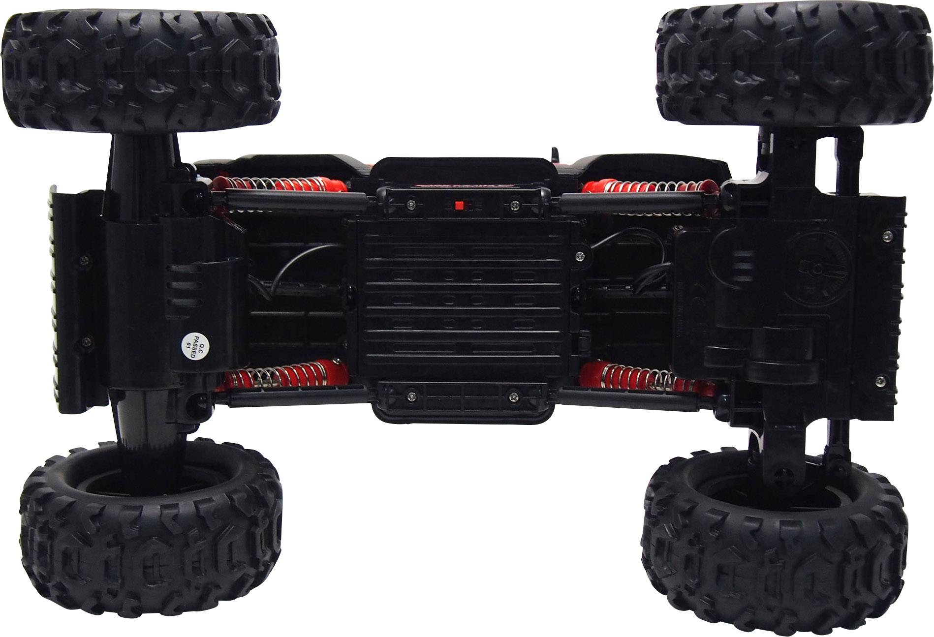 Voiture télécommandée couchée sur le dos, montrant de grandes roues tout-terrain et une suspension. Châssis noir avec des accents rouges.