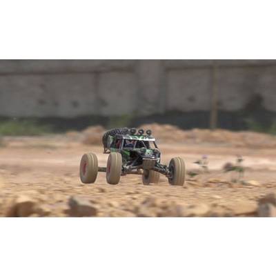 Une voiture télécommandée roule à grande vitesse sur un terrain accidenté et rocailleux. Un mur flou est visible en arrière-plan.