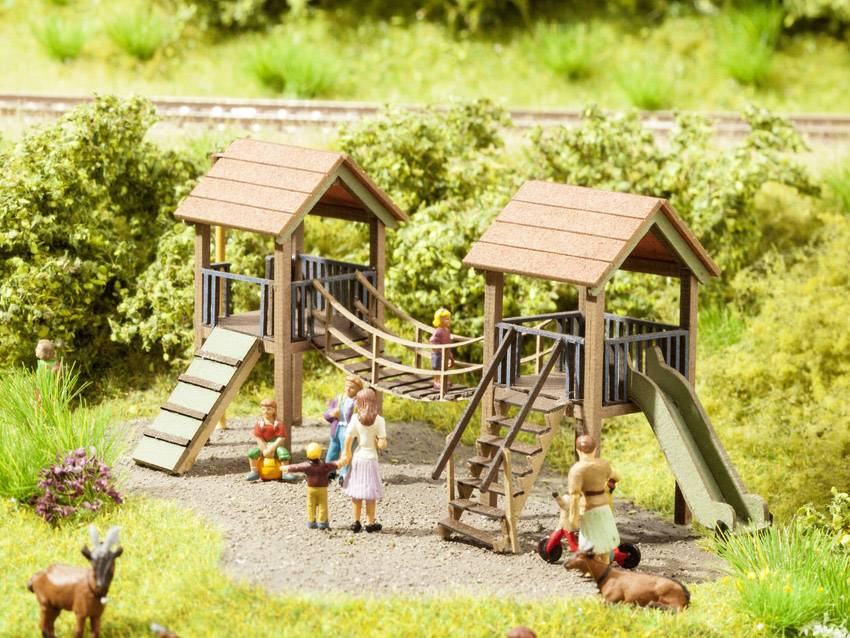 Un paysage de modèle miniature représente une aire de jeux avec une structure d'escalade. Plusieurs personnages, dont des enfants et des adultes, sont visibles.