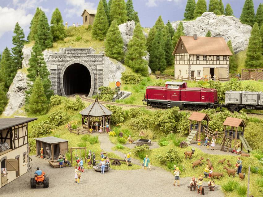 Scène de train miniature avec un train sortant d'un tunnel, entouré de personnages miniatures, d'animaux et de bâtiments, dans un paysage rural.