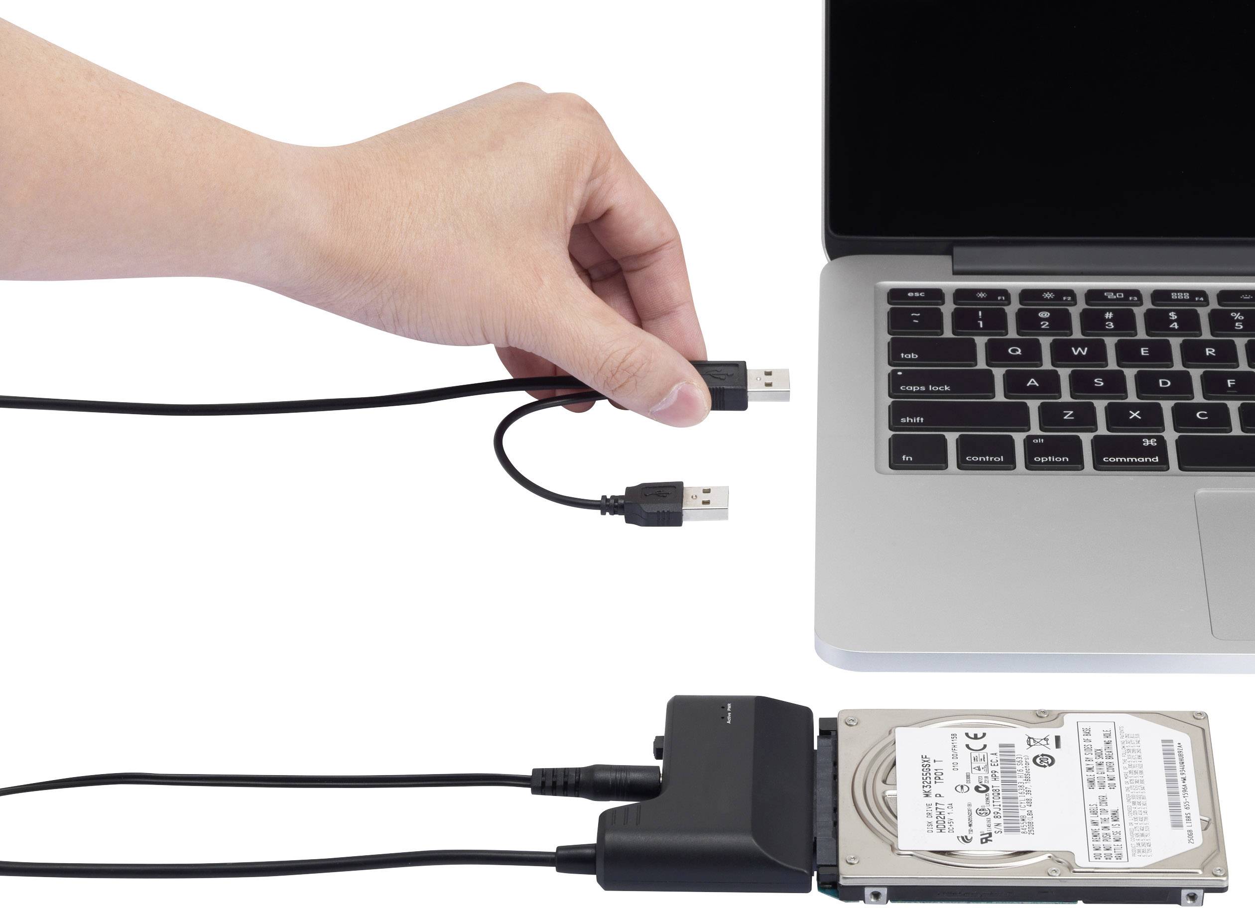 Une main tient un câble USB au-dessus d'un ordinateur portable, à côté duquel se trouve un disque dur externe, connecté via un adaptateur à un second câble USB.