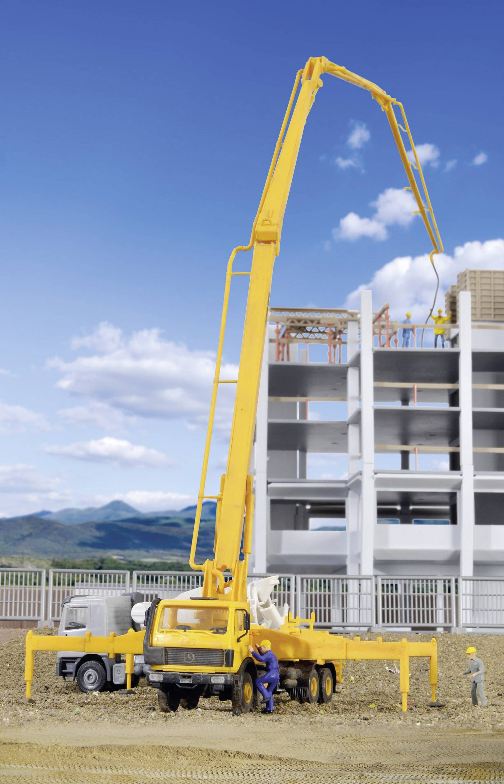 Un grand camion-pompe à béton jaune, avec sa flèche déployée, effectue des travaux de bétonnage sur un immeuble en construction.