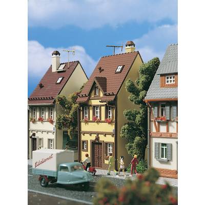 Plusieurs maisons à colombages miniatures avec des figurines humaines sur un trottoir ; une camionnette miniature est garée devant.