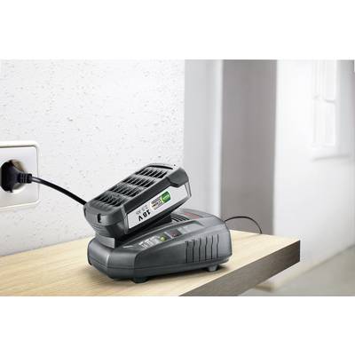 Un chargeur de batterie charge une batterie de 28V sur une table. L'appareil est branché à une prise électrique.
