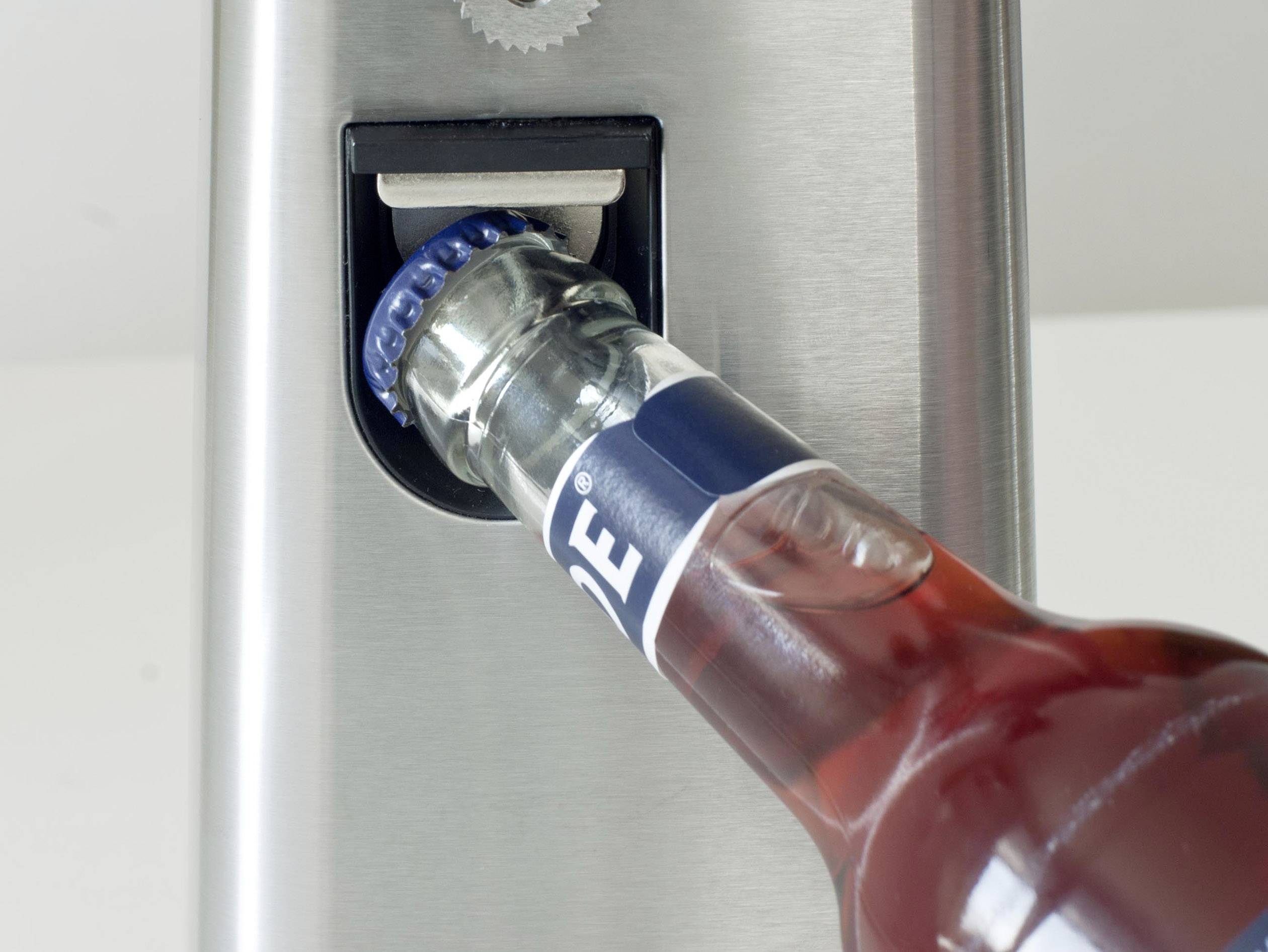 Une bouteille de bière est ouverte avec un décapsuleur argenté.