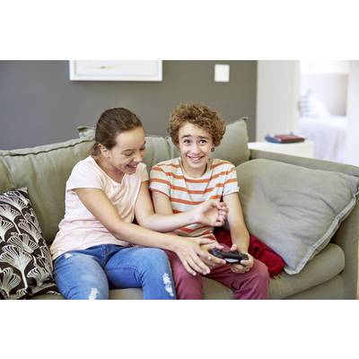 Deux enfants sont assis sur un canapé, riant et jouant à des jeux vidéo avec une manette à la main.
