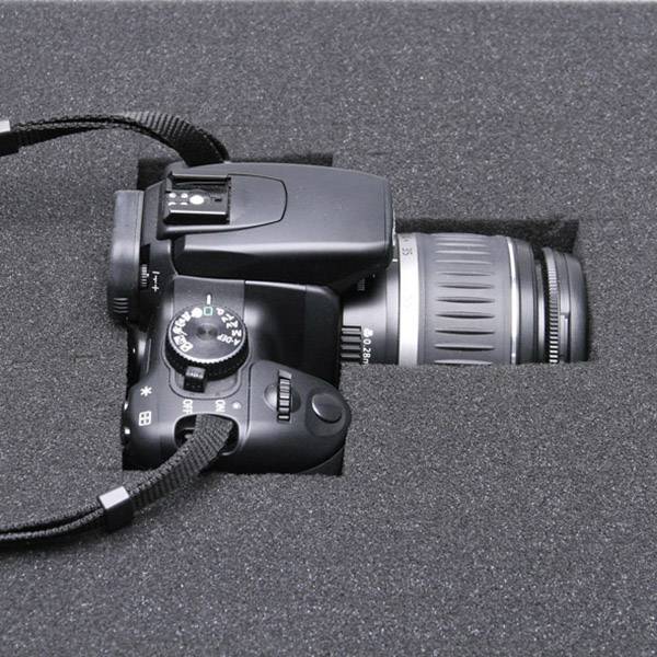 Appareil photo reflex numérique noir dans un emballage en mousse, objectif orienté vers la droite.