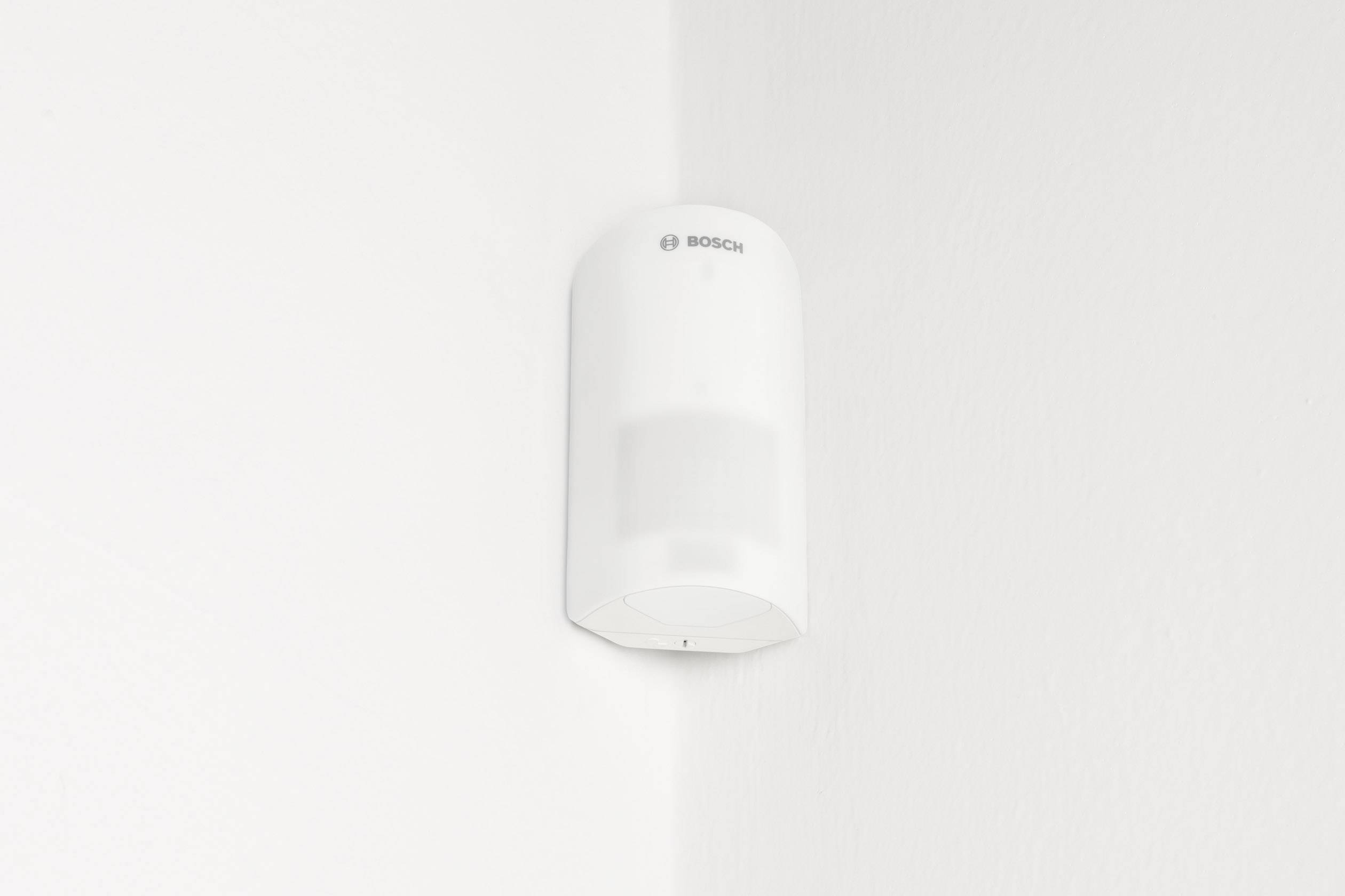 Un détecteur de mouvement blanc est installé dans l'angle d'un mur blanc.