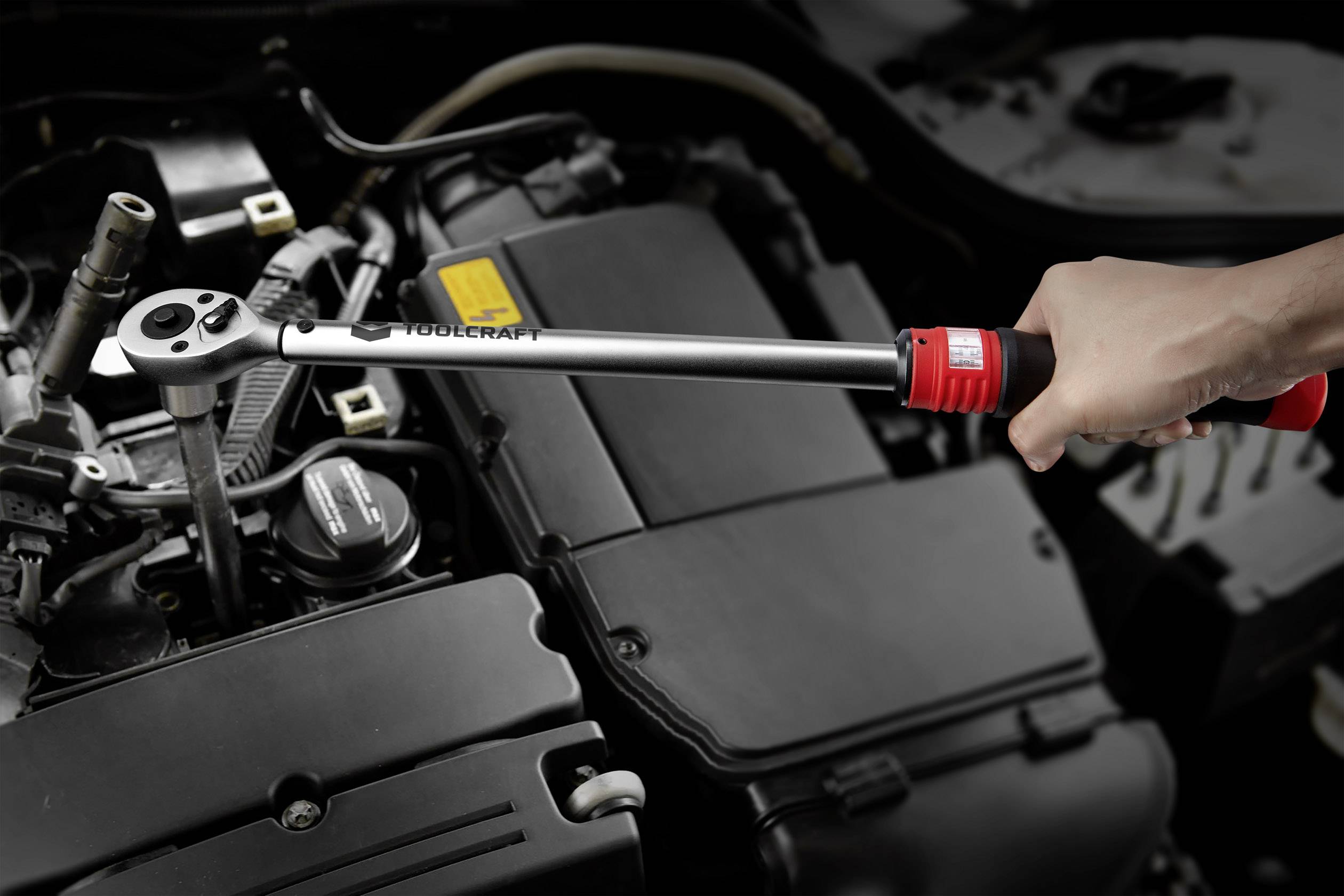 Une clé dynamométrique est tenue dans une main et appliquée sur le moteur d'une voiture.