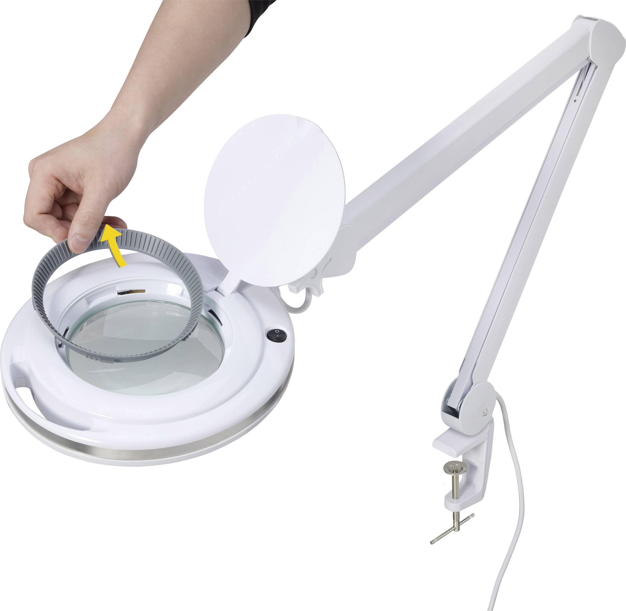 Une main fixe un composant circulaire sur une loupe à bras articulé, montée sur une table.