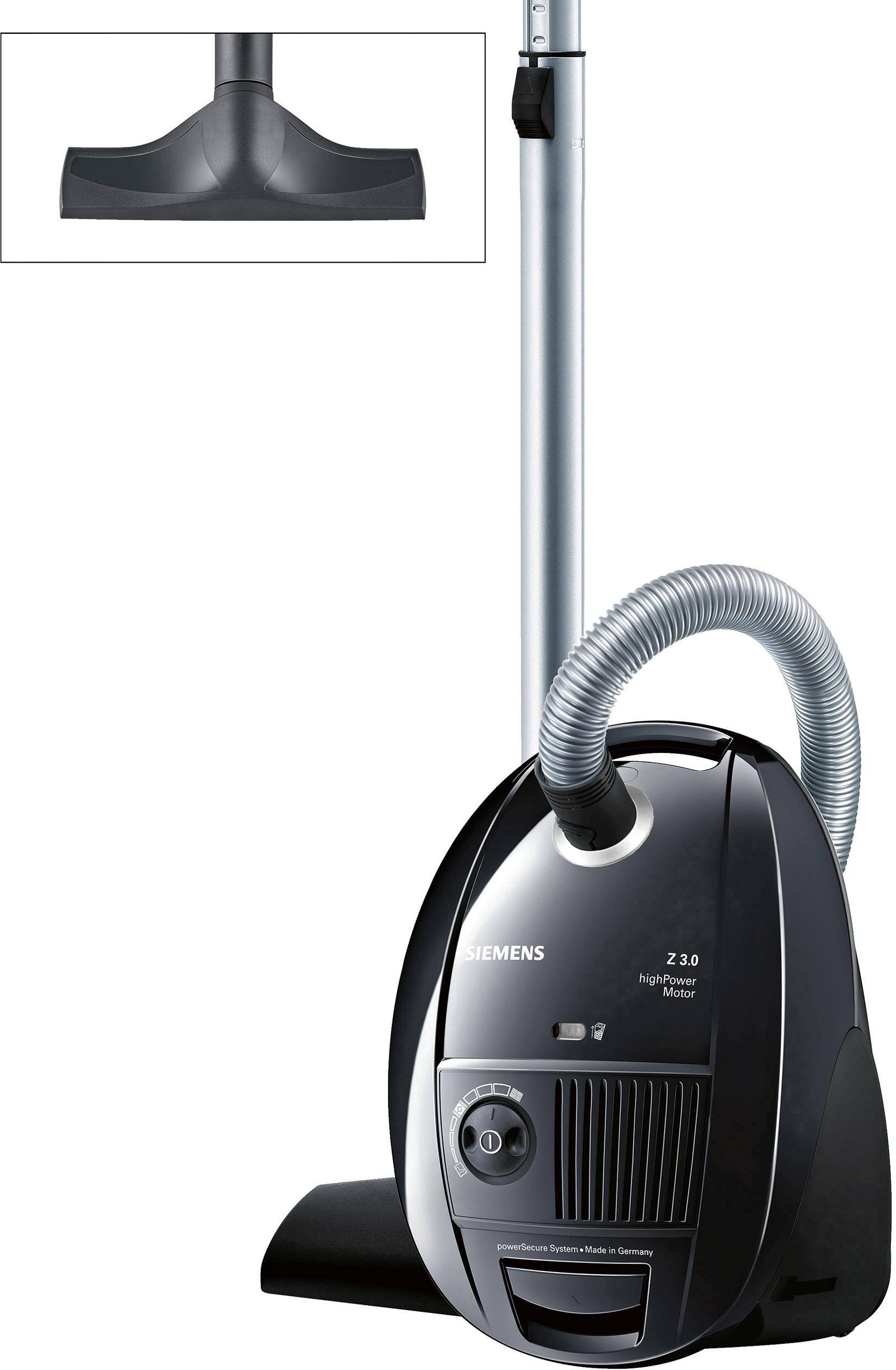 Aspirateur avec prise électrique, tuyau et buse de sol. Le modèle présente un boîtier noir avec des éléments argentés.