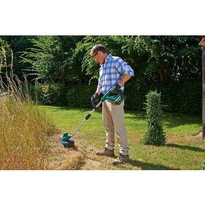 Une personne tond l'herbe avec un coupe-herbe électrique sur une pelouse verte. Des arbustes sont visibles en arrière-plan.