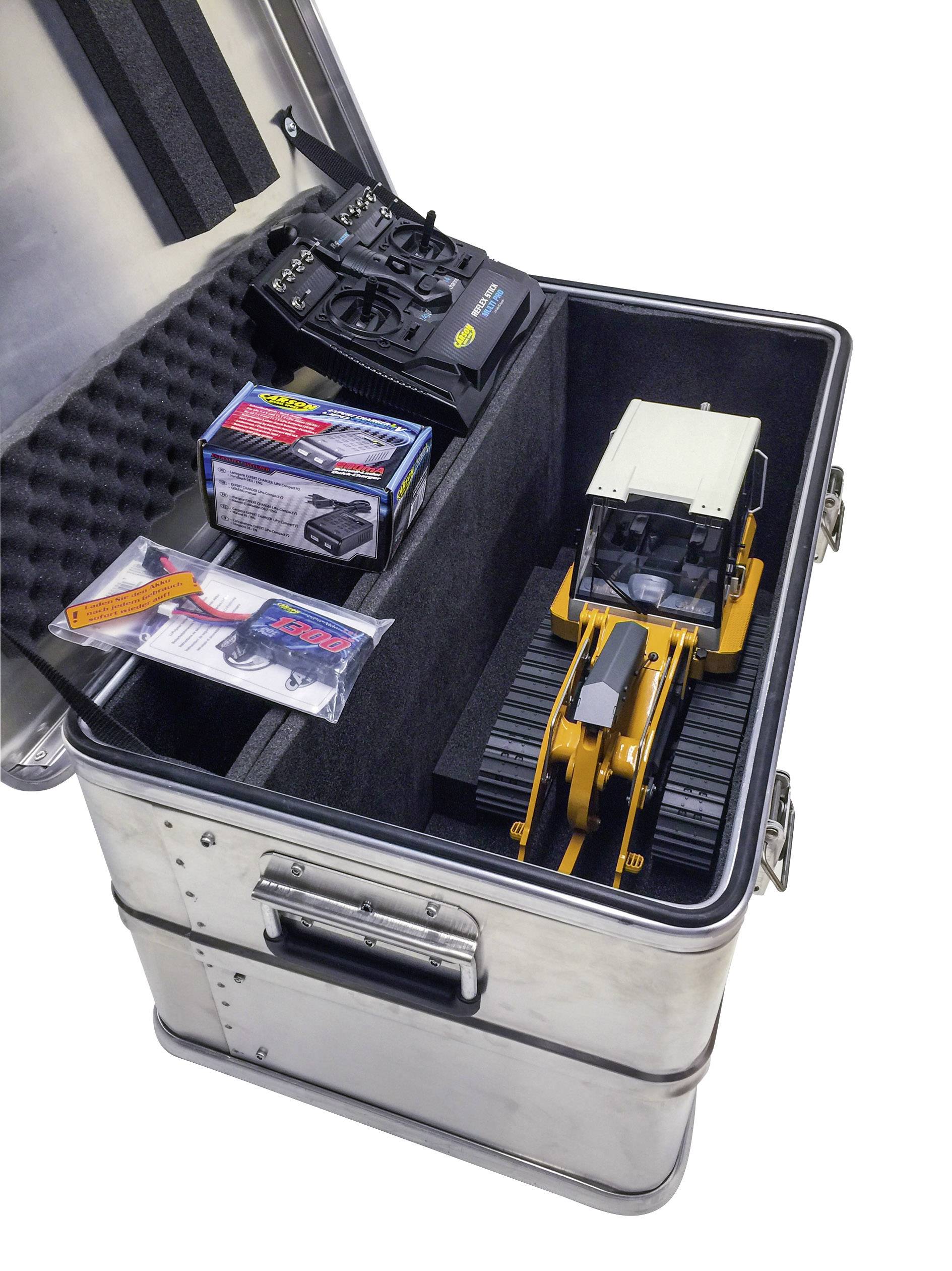 Un excavateur-jouet dans un coffret métallique à côté de télécommandes et d'accessoires, prêt pour le transport ou le rangement.