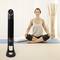 Une femme est assise en tailleur sur un tapis de yoga, à côté d'un ventilateur sur pied. Elle a l'air détendue.