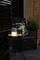 Un haut-parleur portable illuminé est posé sur une table à côté d'une chaise décorée de motifs floraux sur une terrasse au crépuscule.