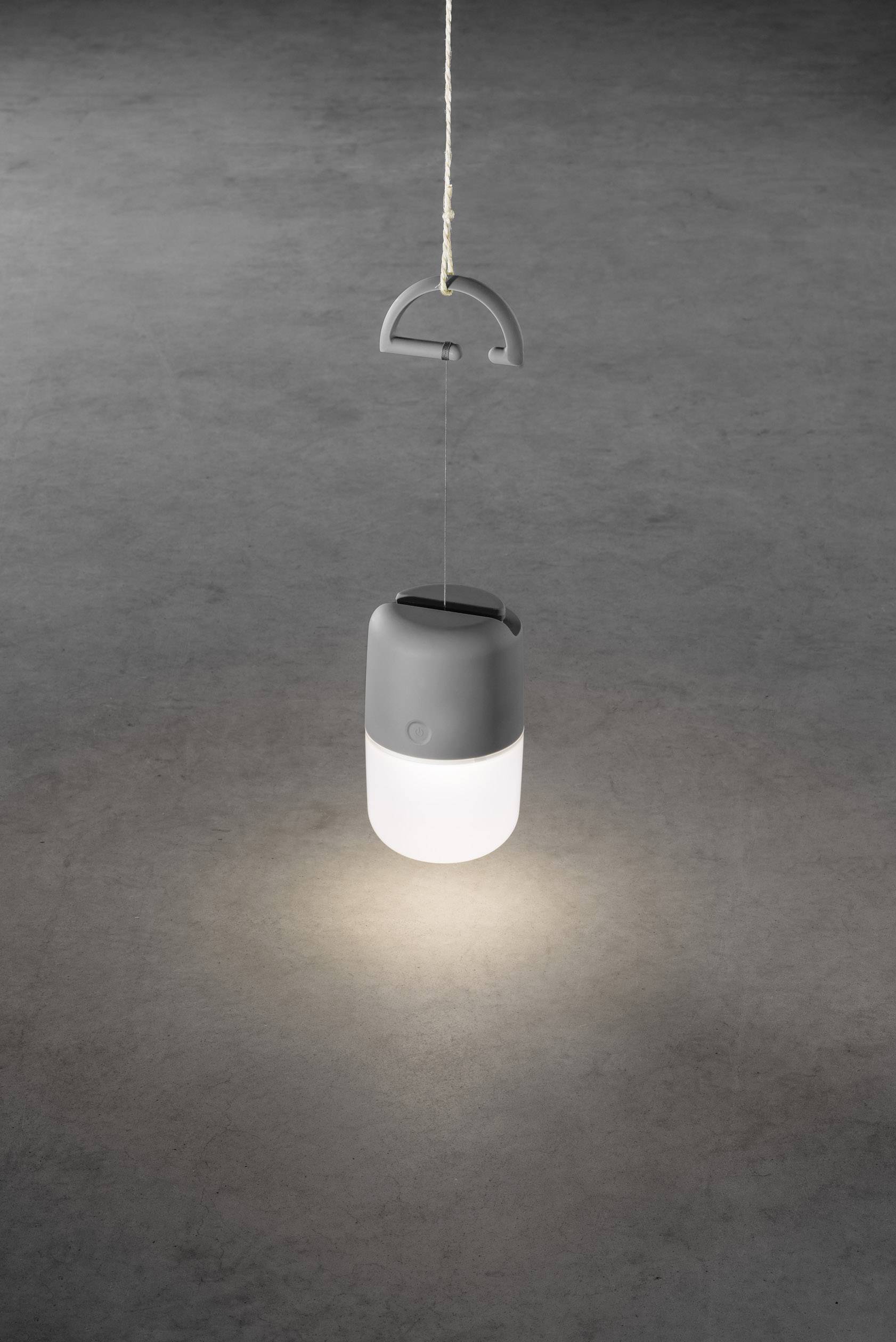 Une lampe grise suspendue éclaire une zone circulaire sur un sol sombre.
