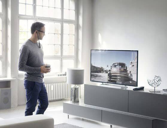 Un homme se tient avec une tasse à la main et regarde un téléviseur affichant une image en noir et blanc d'une voiture.