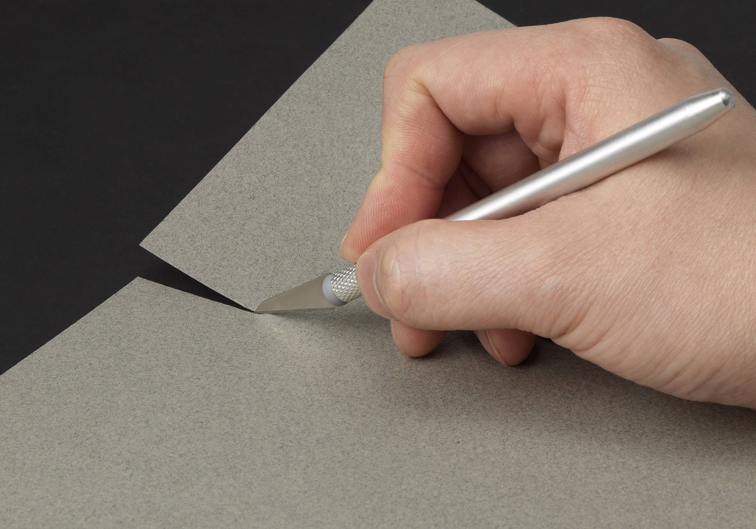 Une main découpant une feuille de papier grise avec un couteau-scalpel argenté.