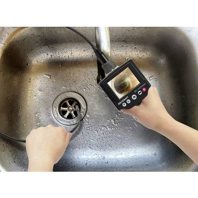 Une personne tient un endoscope au-dessus d'un évier humide et examine les canalisations sur l'écran de l'appareil.