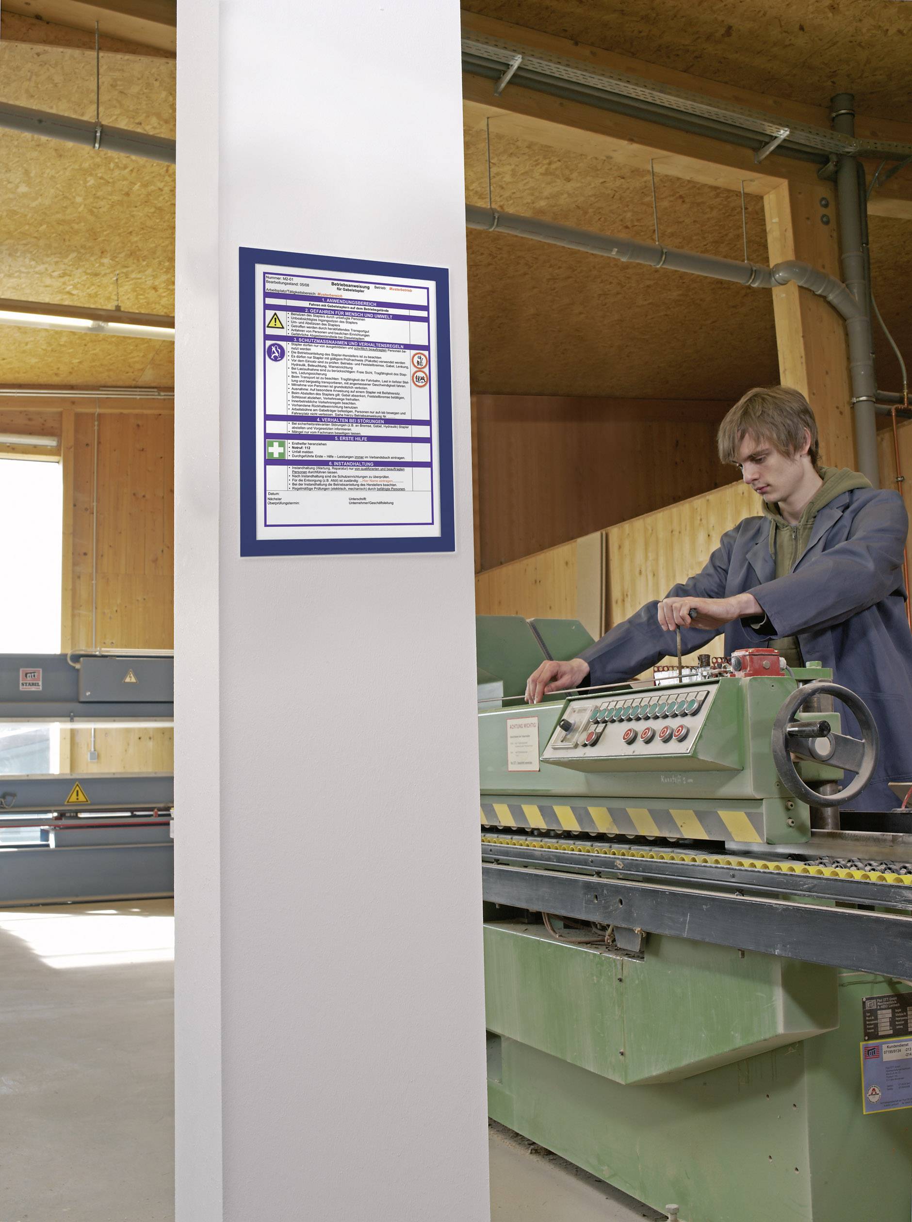 Une personne utilise une machine de transformation du bois verte dans un atelier. Des instructions de sécurité sont affichées sur un pilier.