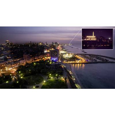 Vue sur une ville côtière illuminée la nuit, avec un accent sur un bâtiment éclairé sur une colline en arrière-plan.