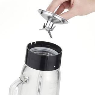 Une personne maintient un embout de mixeur au-dessus d'un pichet en verre pour l'insérer dans le couvercle.