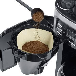 Machine à café avec le compartiment à filtre ouvert, rempli de poudre de café. Une cuillère doseuse contient du café en poudre à côté.