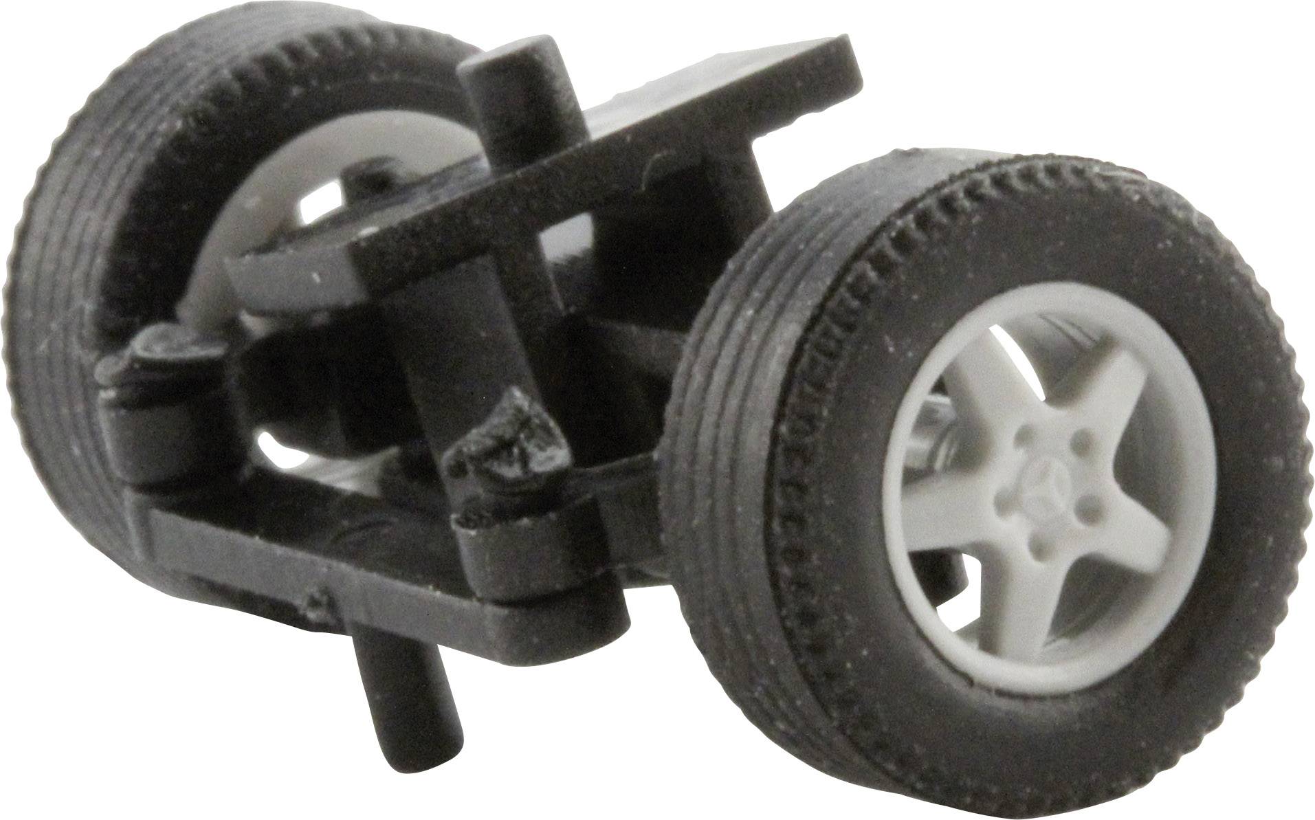 Deux roues de jouet noires avec des jantes blanches sont reliées par un essieu en plastique noir, sur une surface blanche.