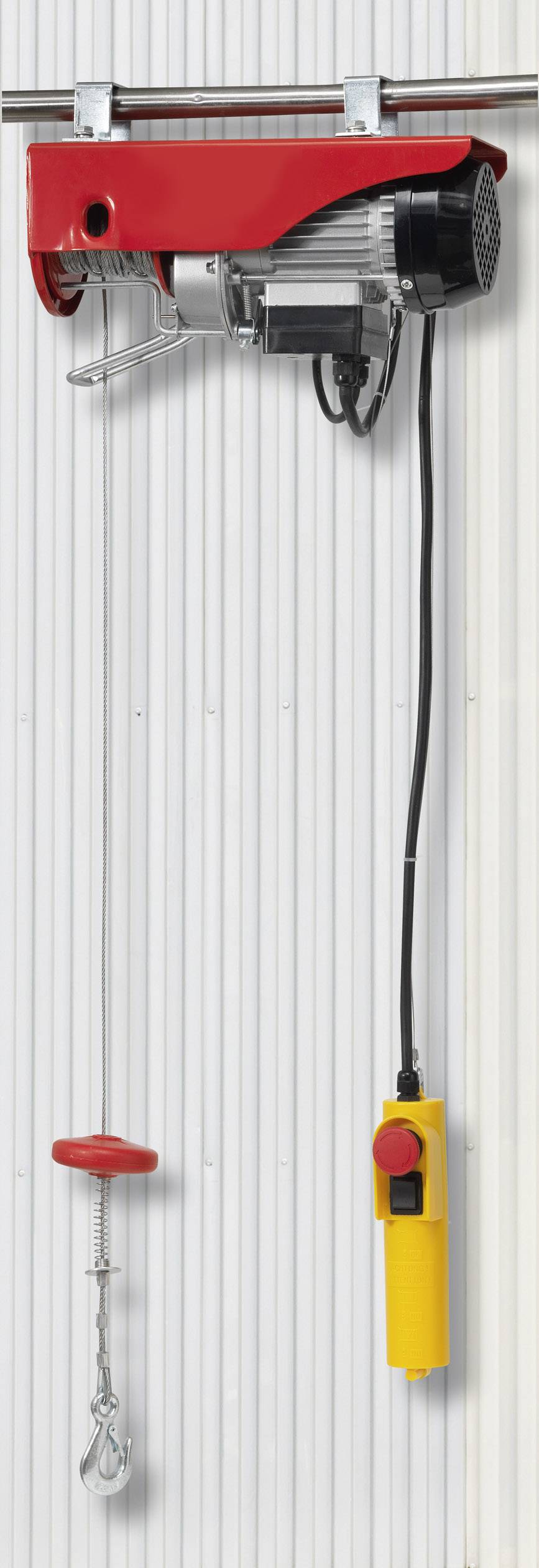 Un treuil électrique à boîtier rouge est fixé sur un rail métallique. En dessous pend une télécommande à poignée jaune.