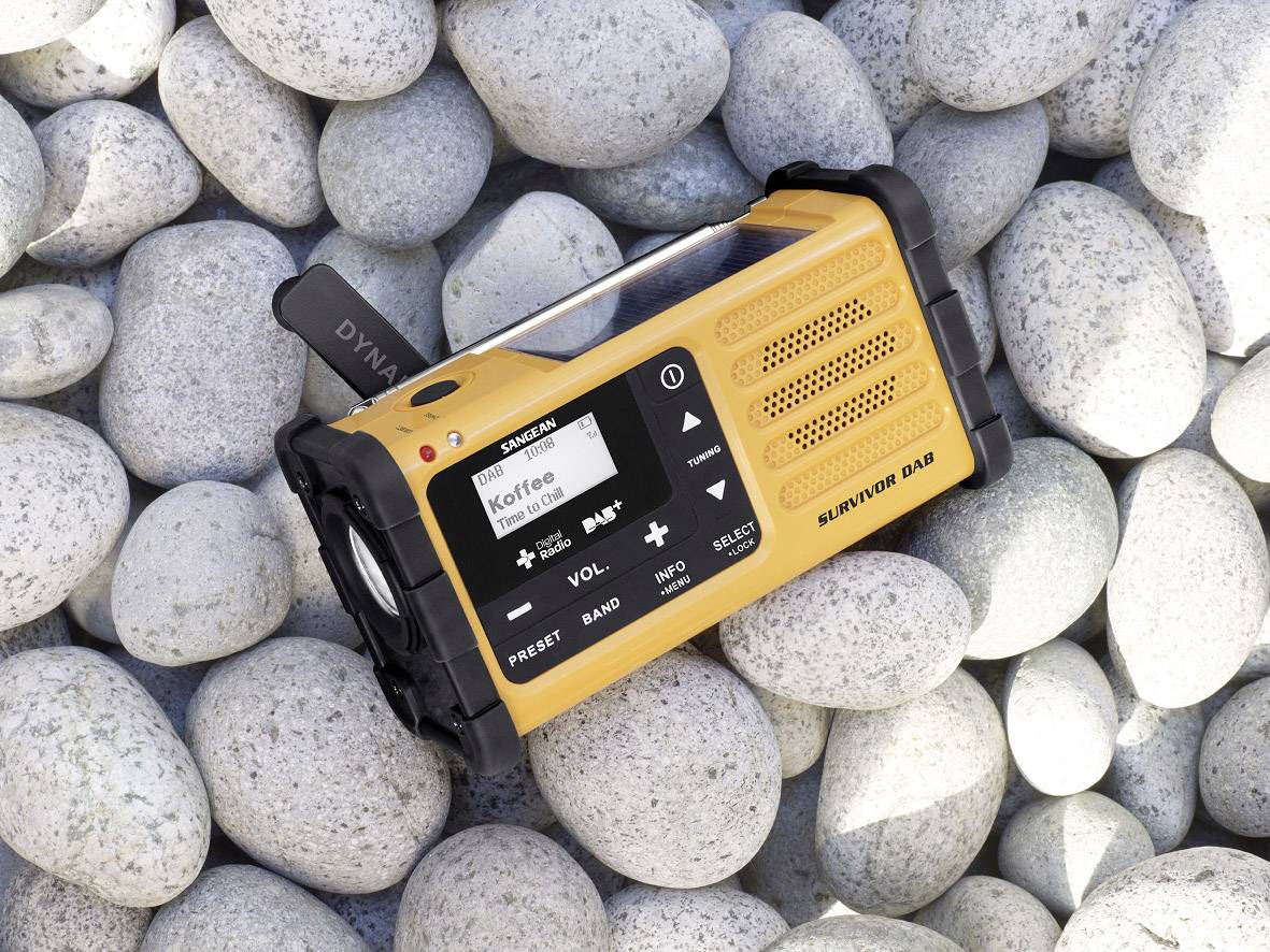 Une radio portative jaune est posée sur des galets clairs. Sur l'écran est affiché le mot 'Café'. En haut à gauche se trouve une antenne télescopique.