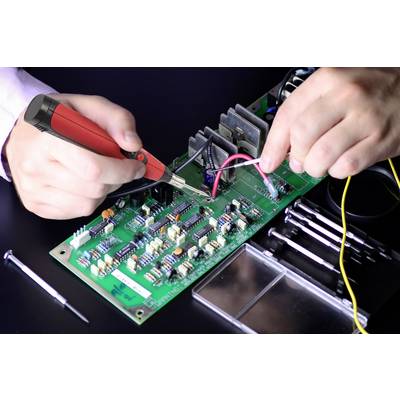 Une personne soude avec un fer à souder sur une carte électronique verte, entourée d'outils.