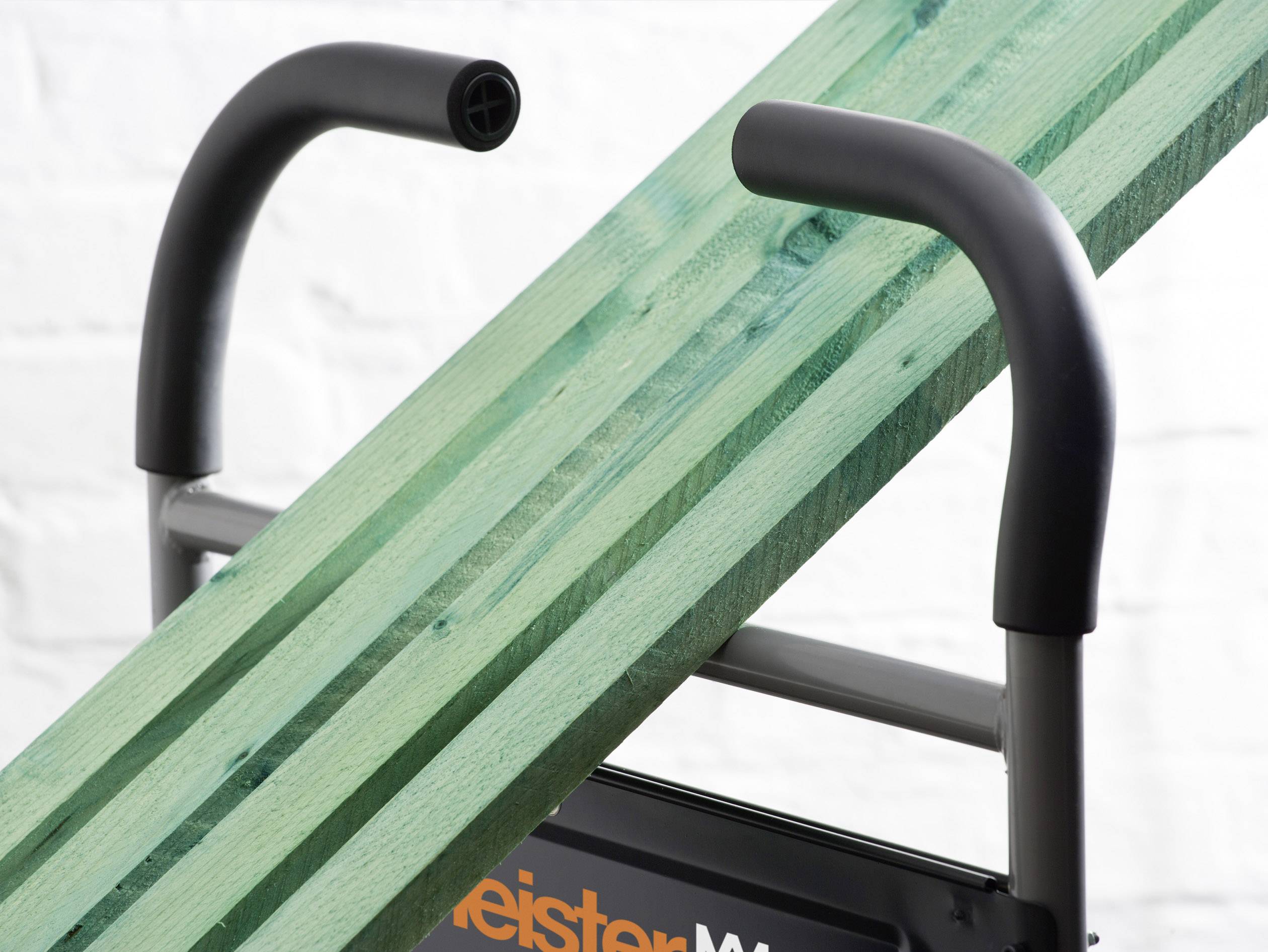 Une planche verte en bois est posée en diagonale sur un support métallique gris avec des poignées dans une pièce lumineuse.