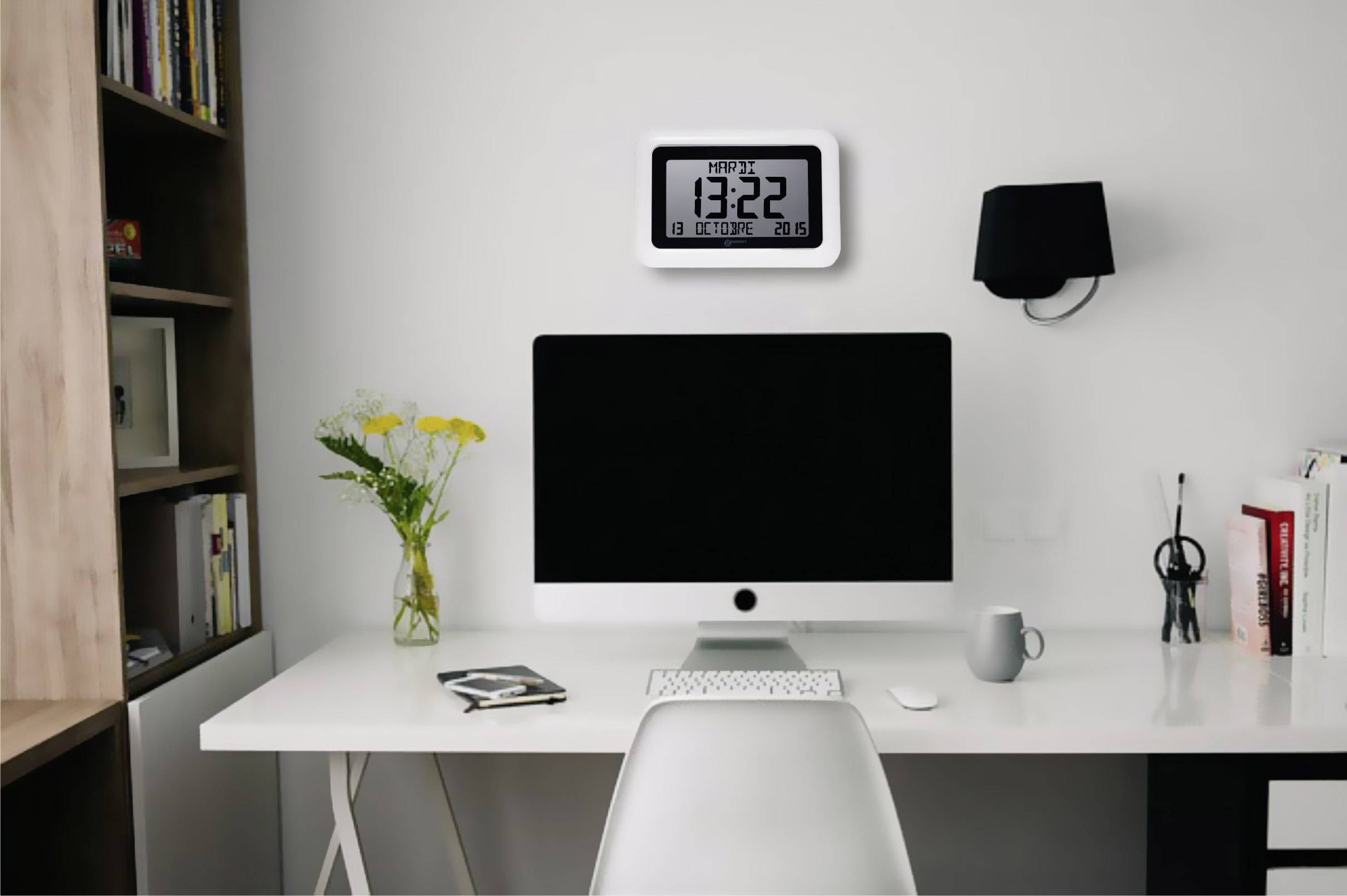 Un bureau avec un ordinateur, un vase de fleurs, une lampe murale et une horloge numérique affichant 13:22.