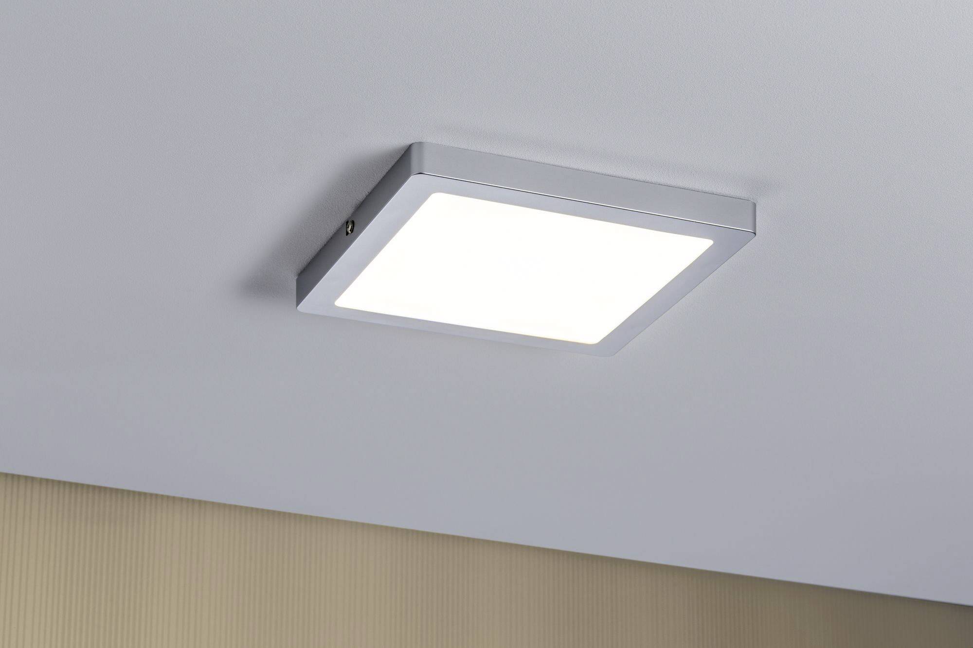 Un plafonnier carré avec un cadre argenté diffuse une lumière blanche uniforme. Il est installé sur un plafond lisse et clair.