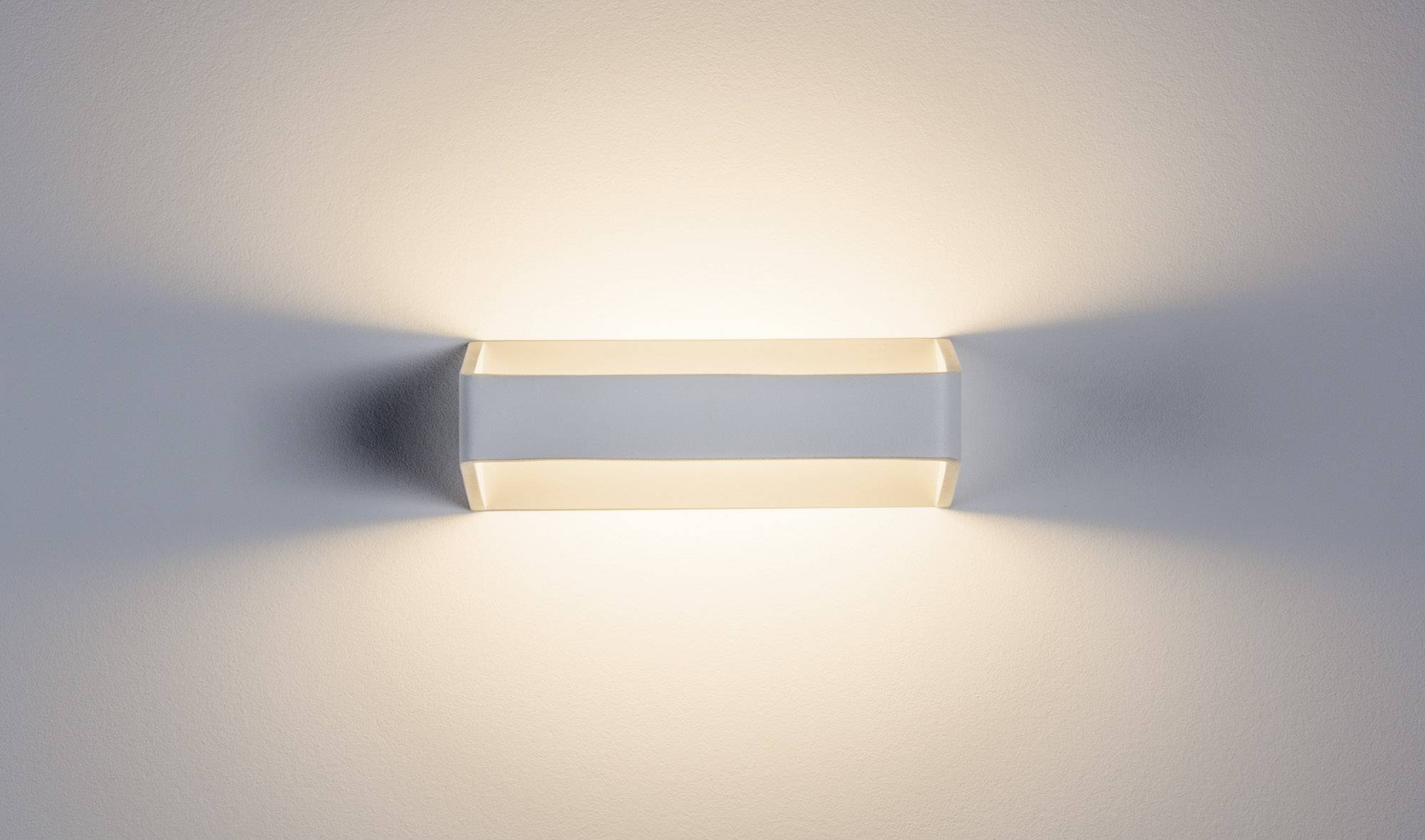 Un luminaire mural moderne de forme rectangulaire diffuse une lumière chaleureuse vers le haut et vers le bas, crée des ombres douces et apporte une ambiance apaisante.