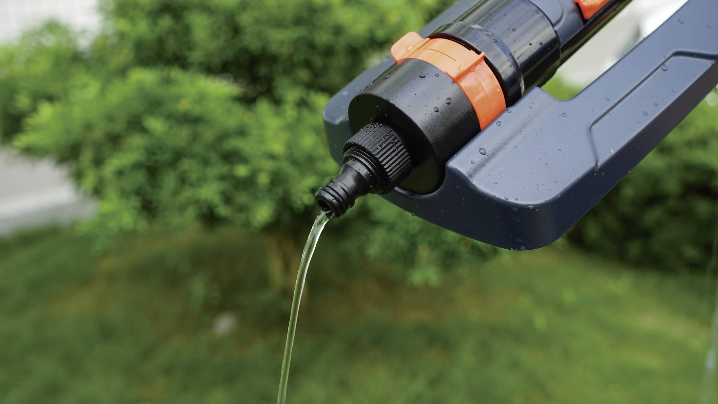 Un robinet au design noir et orange arrose des plantes vertes en arrière-plan, illustrant l'irrigation.