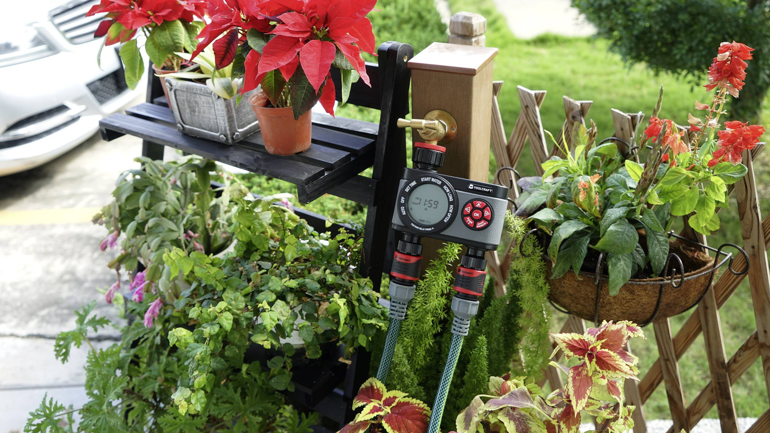 Un coin de balcon avec des fleurs rouges en fleurs, un système d'irrigation par eau et un feuillage vert luxuriant en arrière-plan.