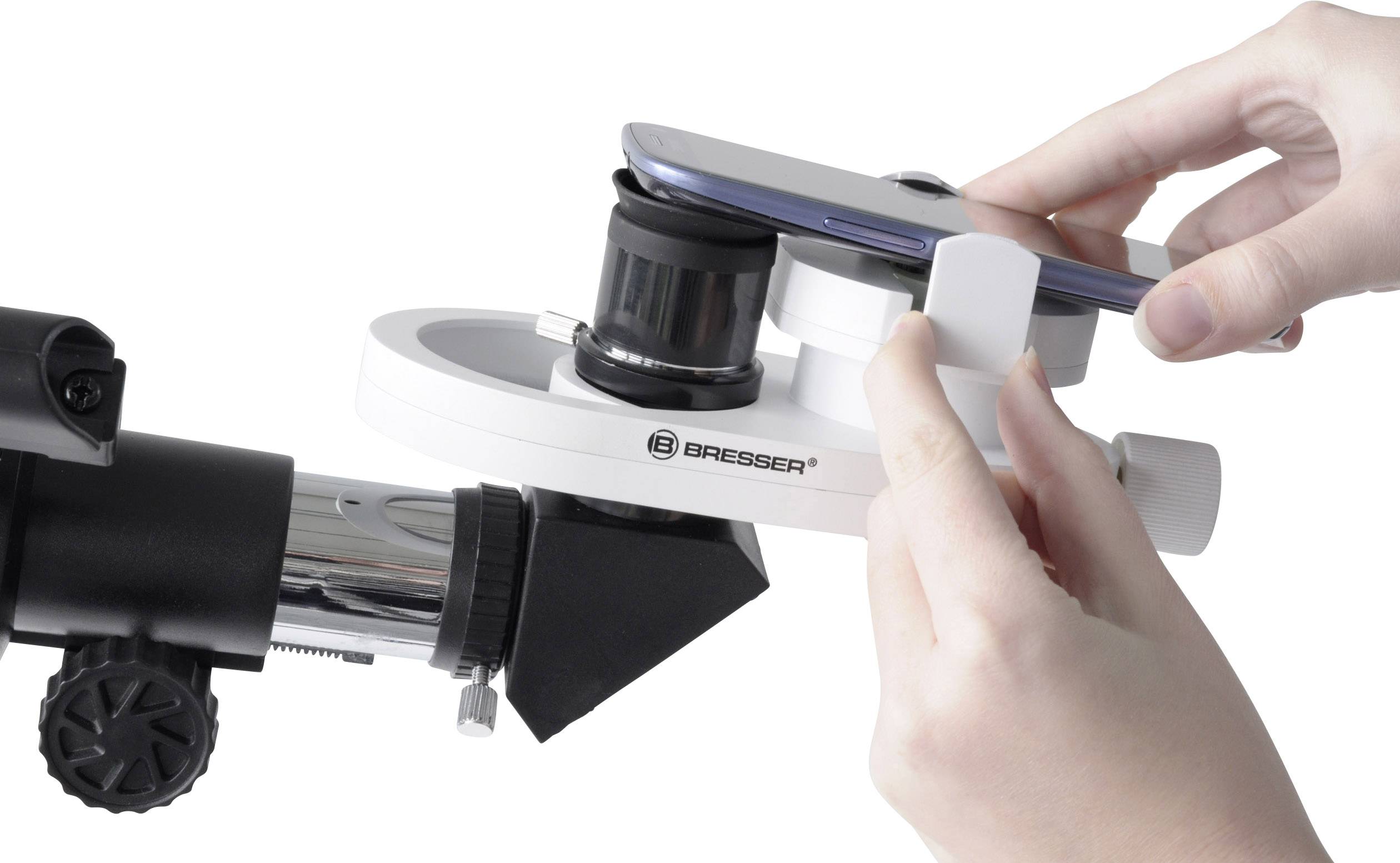 Un smartphone est monté sur un télescope à l'aide d'un adaptateur pour prendre une photo à travers l'oculaire. Des mains ajustent l'adaptateur.