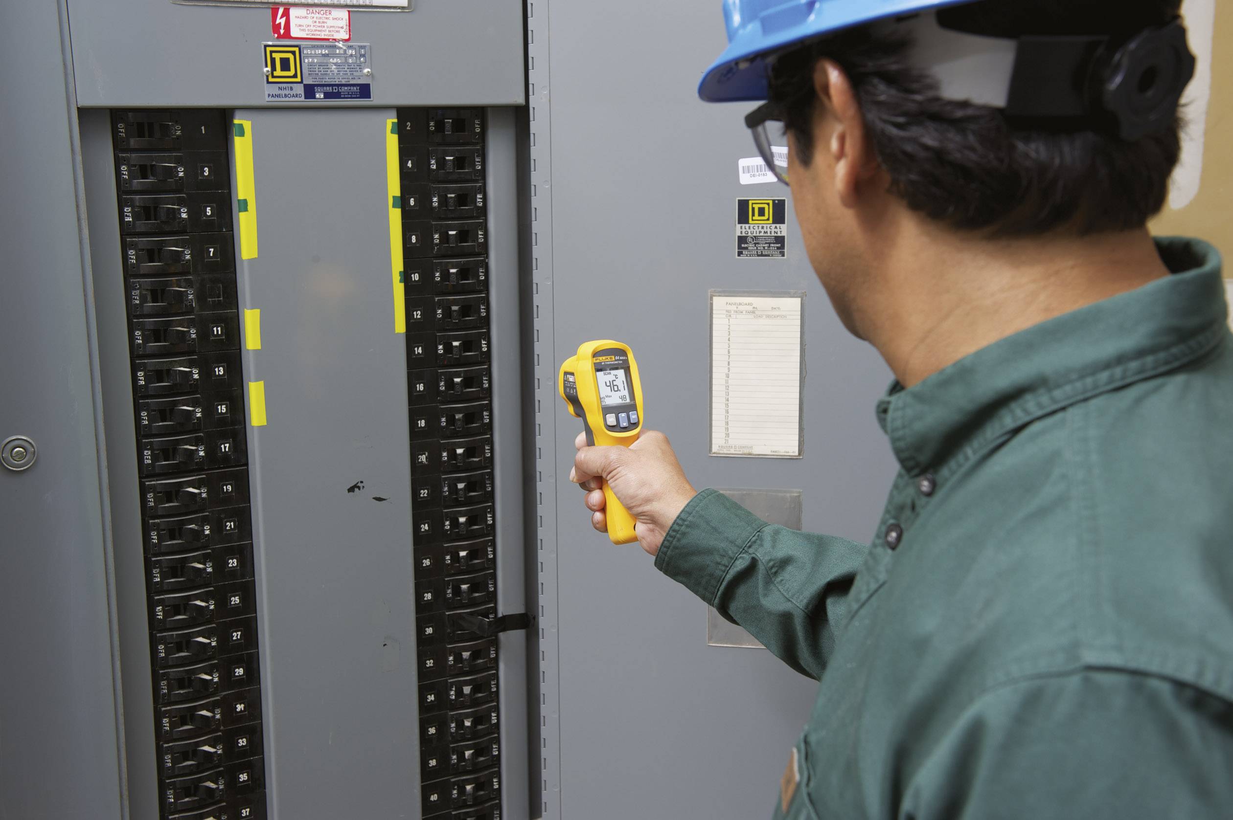 Un technicien vérifie un tableau électrique à l'aide d'un thermomètre infrarouge afin de garantir la sécurité thermique des composants électriques.