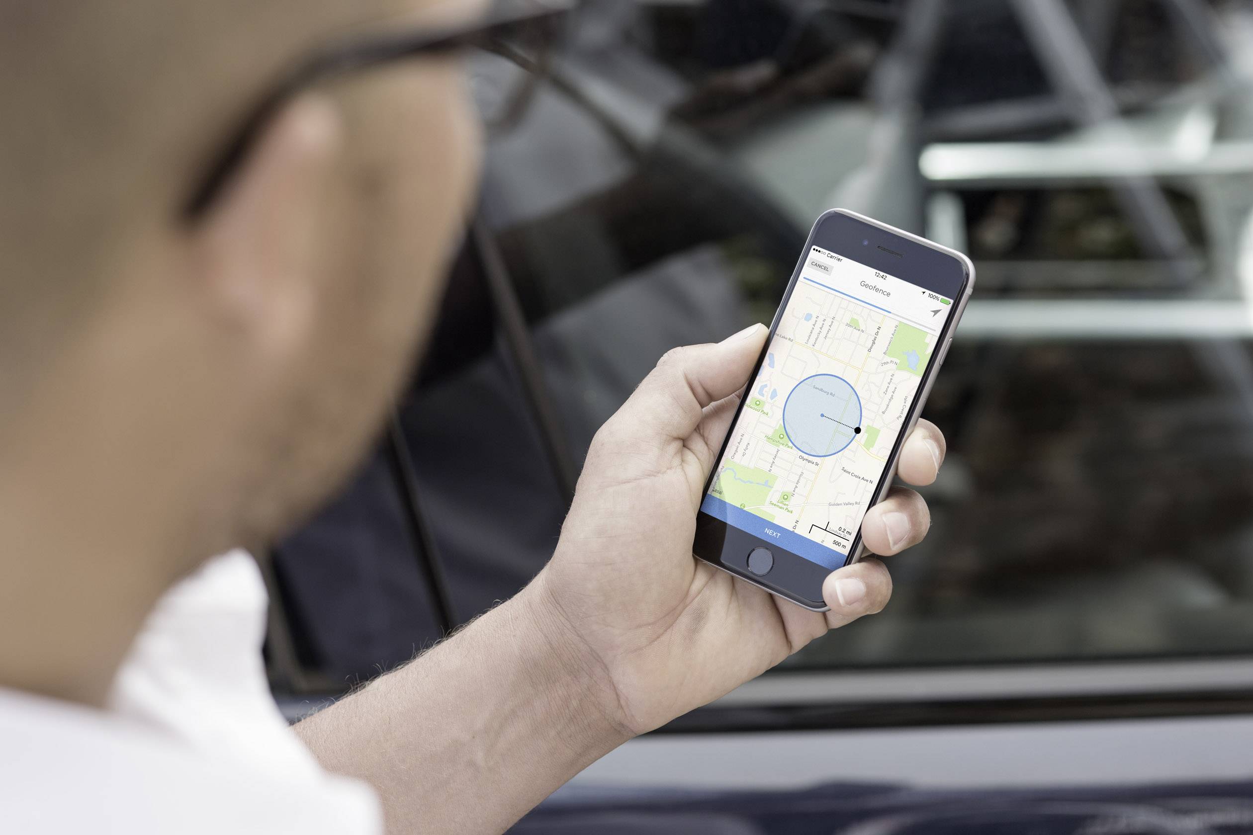 Une personne tient un smartphone avec une application de cartes ouverte, mettant l'accent sur un cercle bleu indiquant la localisation. En arrière-plan, on aperçoit un véhicule flou.