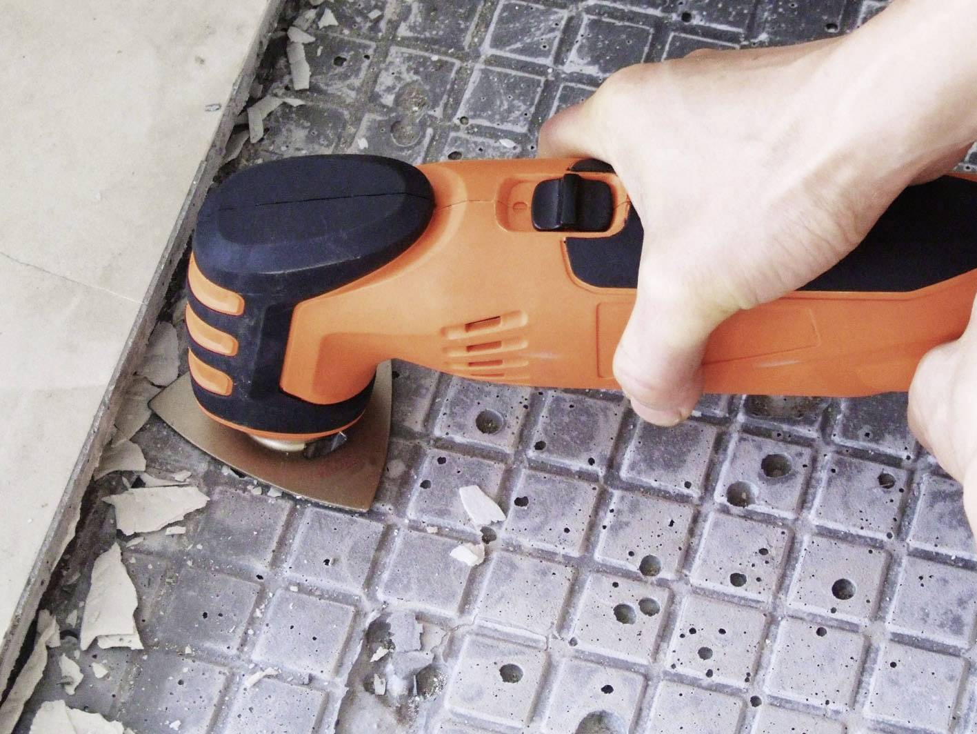 Une personne utilise un outil électrique orange pour enlever des carreaux sur un sol.