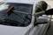 Une personne nettoie le pare-brise d'une voiture blanche avec un long balai sur un parking.