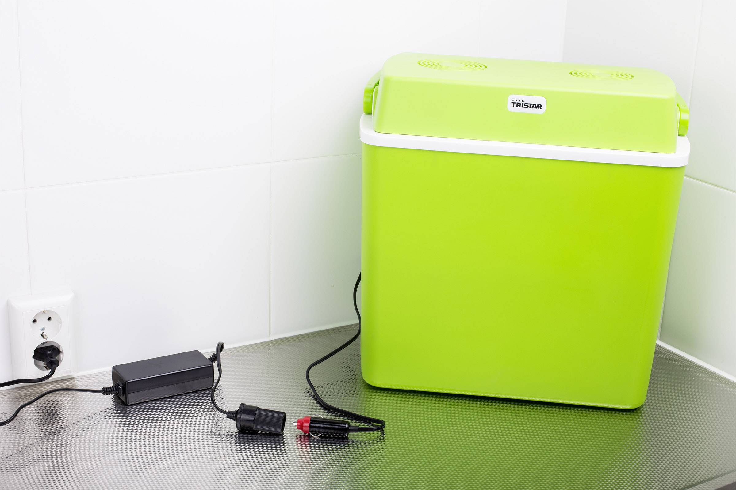 Glacière portable verte posée sur un plan de travail de cuisine, branchée à une prise électrique. Adaptée pour le camping et les voyages.